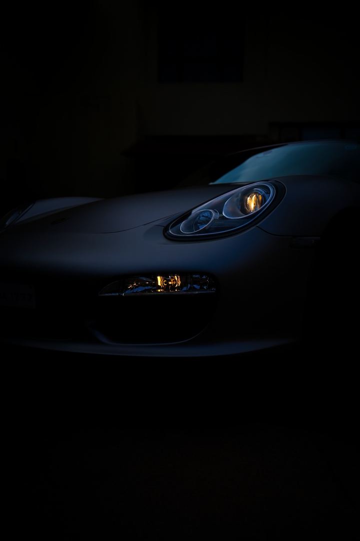 A single Porsche headlight glowing in a dark studio.