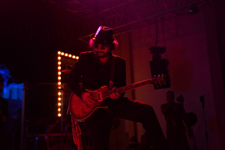 Guitarist in a hat plays under red light.
