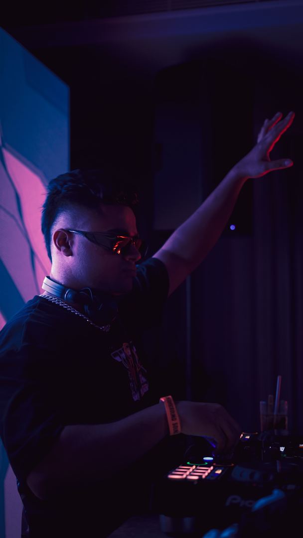 DJ raises one arm under purple light.