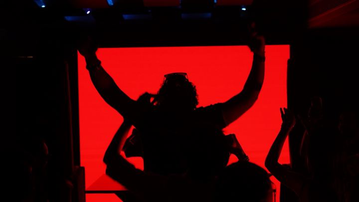 Silhouette of a performer with raised arms against a red screen.