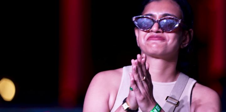 Guest in tinted glasses smiles with hands pressed together.