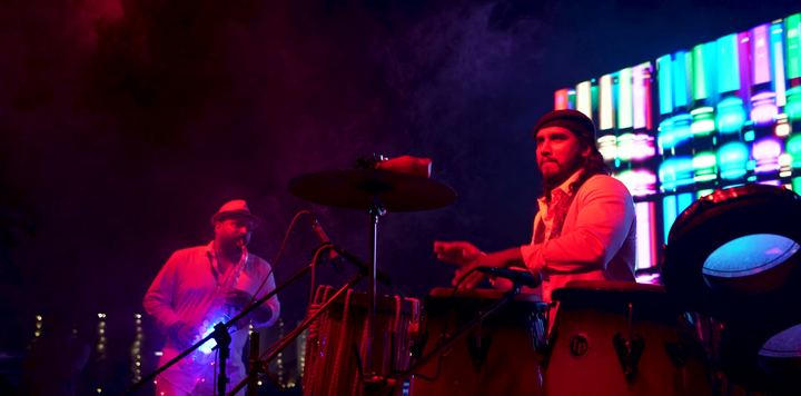 Percussionists play under magenta and cyan light.