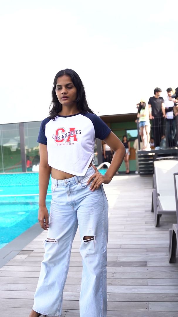 Contestant poses in a baseball tee and wide jeans by the pool.