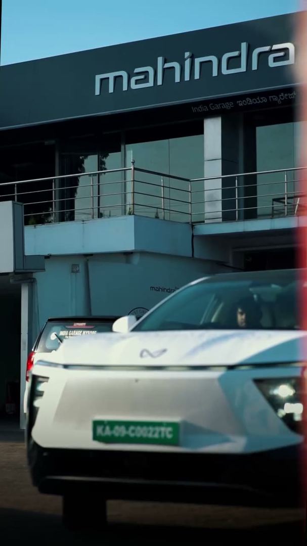 White electric SUV parked in front of a Mahindra showroom.