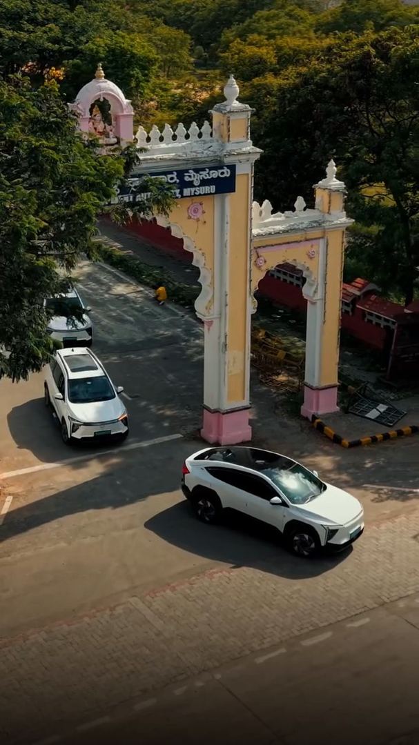 Aerial view of two electric SUVs passing a palace gate.
