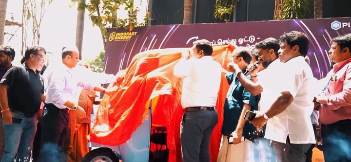 Guests pull the red cover off the new vehicle outdoors.