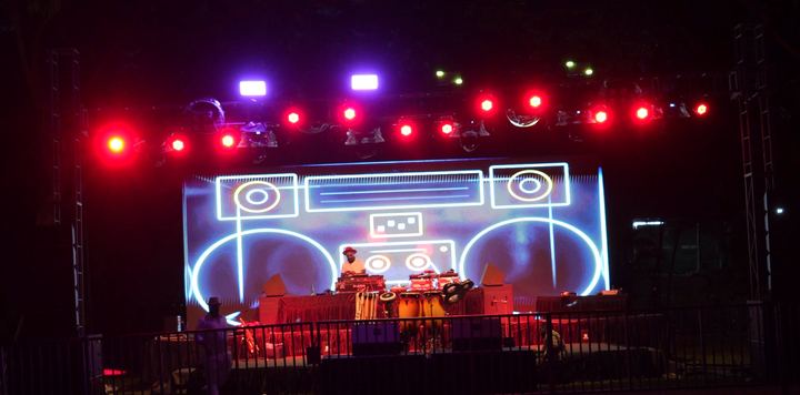 Open-air stage with a neon boombox outline and red lights at night.