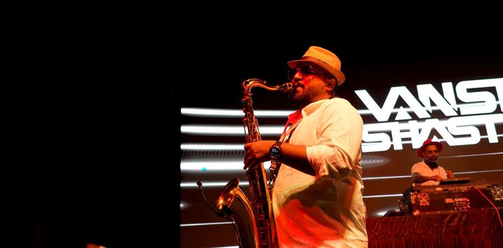 Saxophonist in a hat plays beside the DJ booth.
