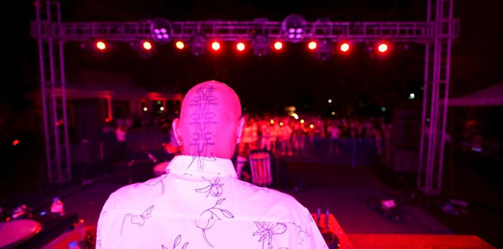 DJ seen from behind, facing a crowd under pink stage lights.
