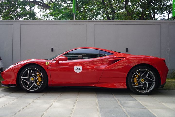 Red Ferrari with race number 21 parked by a concrete wall.